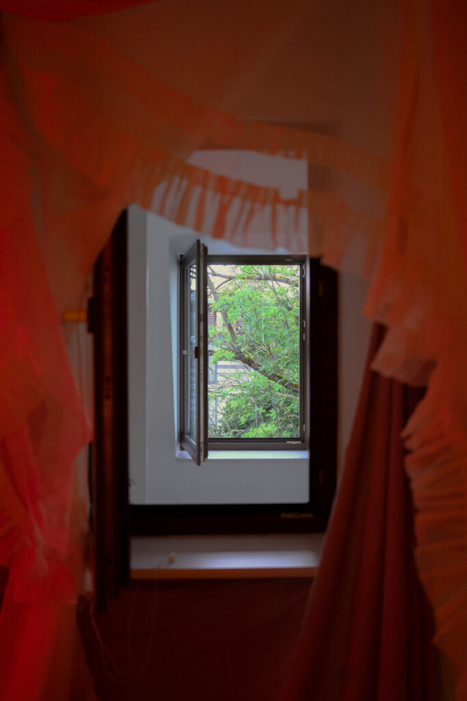 Durch mehrere Stofflagen hindurch sieht man ein offenes Fenster ins Grüne.