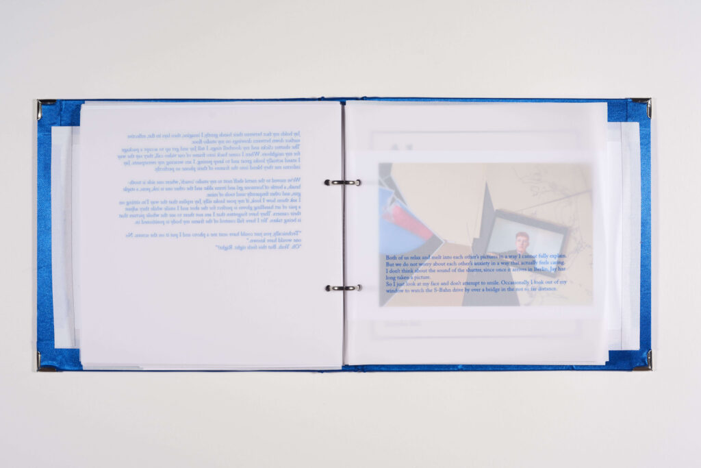 Das Bild zeigt eine aufgeklappte Publikation. Auf der linken Seite ist eine transparente Seite zu sehen, auf der Text steht. Hinter dieser Seite scheint eine Fotografie durch.
